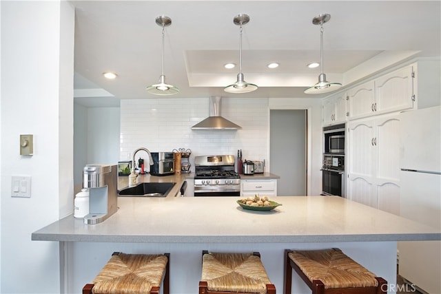 kitchen featuring sink, kitchen peninsula, wall chimney exhaust hood, stainless steel appliances, and a breakfast bar