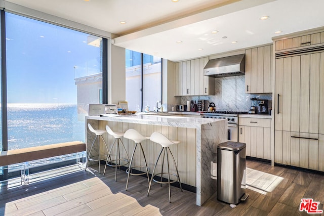 kitchen with backsplash, hardwood / wood-style floors, wall chimney exhaust hood, a breakfast bar, and high end appliances