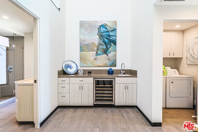 bar featuring washer and clothes dryer, hardwood / wood-style flooring, wine cooler, sink, and white cabinetry