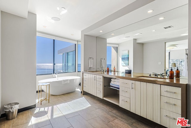 bathroom with vanity, a tub to relax in, a water view, and a wealth of natural light