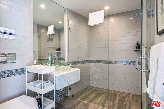 bathroom with a shower with door, tile walls, sink, and toilet