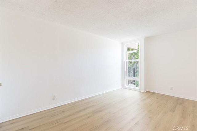 empty room with a textured ceiling and light hardwood / wood-style flooring