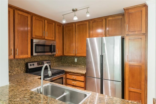 kitchen featuring decorative backsplash, appliances with stainless steel finishes, track lighting, light stone counters, and sink