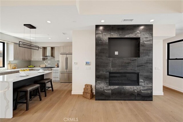 kitchen featuring a breakfast bar, light brown cabinets, wall chimney range hood, decorative light fixtures, and stainless steel refrigerator