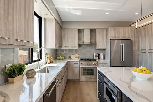 kitchen featuring light brown cabinets, high quality appliances, wall chimney range hood, sink, and light stone counters