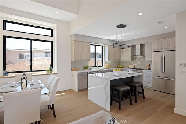 kitchen with a center island, wall chimney range hood, high quality fridge, tasteful backsplash, and decorative light fixtures