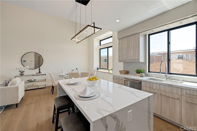 kitchen featuring pendant lighting, sink, light hardwood / wood-style flooring, stainless steel dishwasher, and a kitchen island