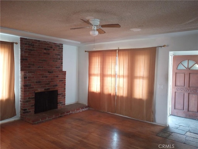 unfurnished living room with a healthy amount of sunlight, hardwood / wood-style floors, a brick fireplace, and a textured ceiling