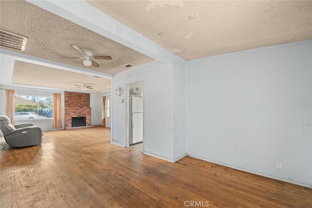 unfurnished living room with ceiling fan, hardwood / wood-style floors, a brick fireplace, and a textured ceiling