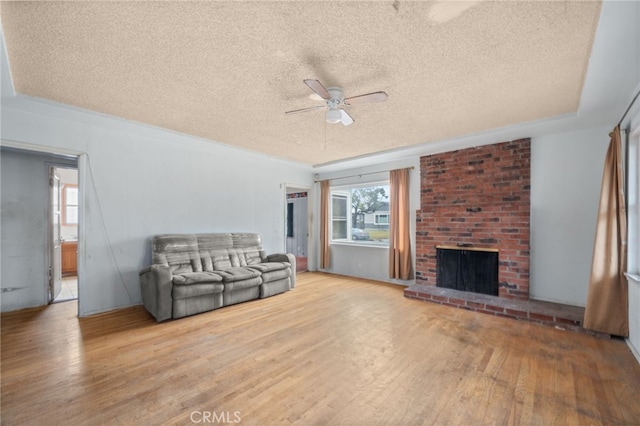 unfurnished living room featuring a brick fireplace, a textured ceiling, light hardwood / wood-style flooring, and ceiling fan