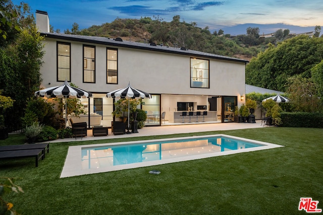 back house at dusk featuring outdoor lounge area, a yard, and a patio