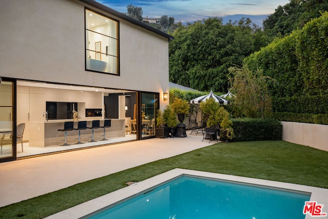 back house at dusk with a lawn and a patio area