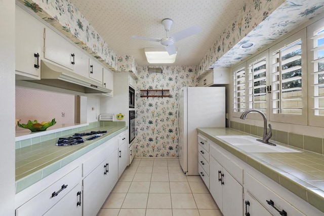 kitchen featuring tile countertops, sink, white appliances, light tile patterned flooring, and white cabinets