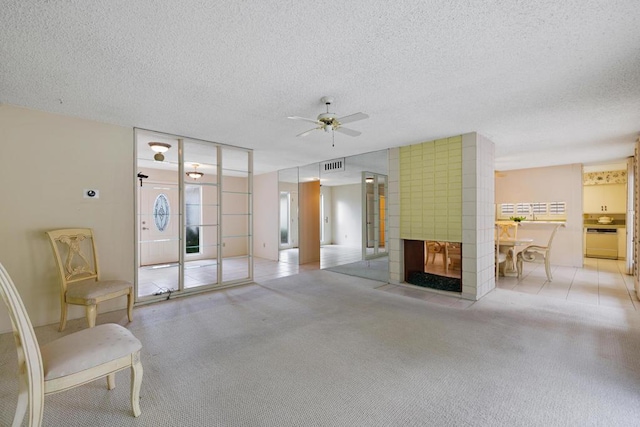 carpeted living room featuring ceiling fan, a tile fireplace, and a textured ceiling