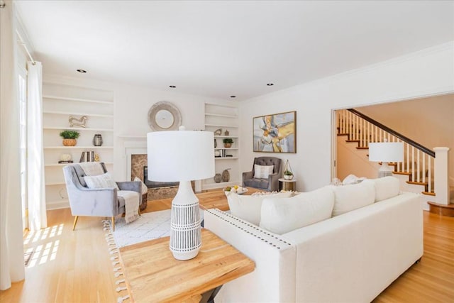 living room featuring ornamental molding, a high end fireplace, light hardwood / wood-style flooring, and built in features