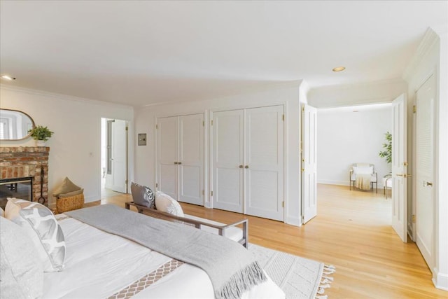 bedroom featuring crown molding, two closets, a fireplace, and light wood-type flooring