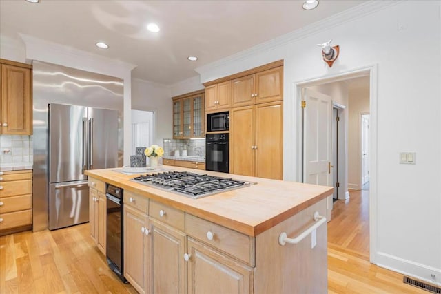 kitchen with butcher block counters, light wood-type flooring, a kitchen island, and black appliances