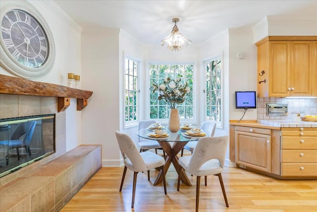 dining space featuring a tiled fireplace, ornamental molding, light hardwood / wood-style floors, and a chandelier