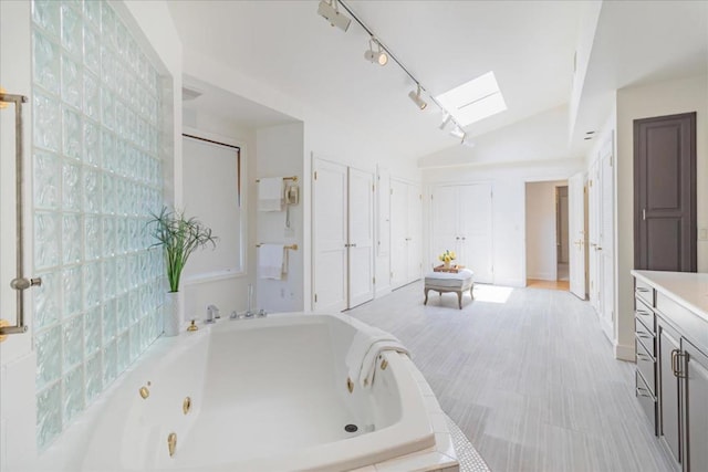 bathroom featuring vanity, lofted ceiling with skylight, and tiled bath