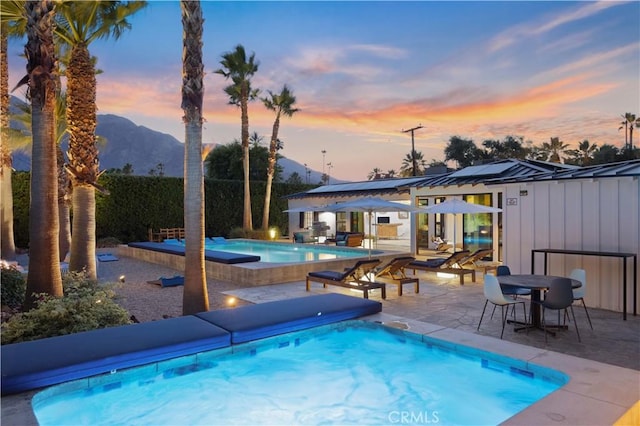 pool at dusk featuring a patio area, an outdoor structure, a hot tub, and a mountain view