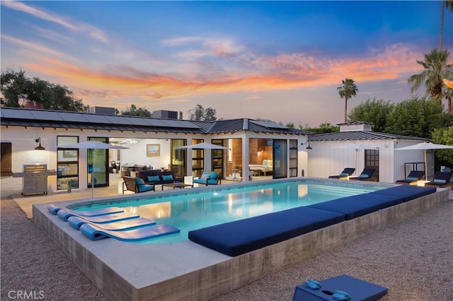 pool at dusk featuring an outbuilding, a patio area, and an outdoor hangout area