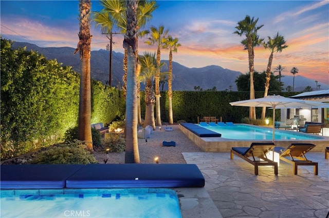 pool at dusk with a mountain view, a jacuzzi, and a patio