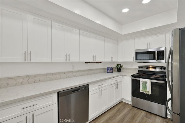 kitchen with recessed lighting, stainless steel appliances, wood finished floors, white cabinets, and light stone countertops