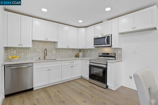 kitchen with sink, white cabinetry, light hardwood / wood-style flooring, backsplash, and appliances with stainless steel finishes