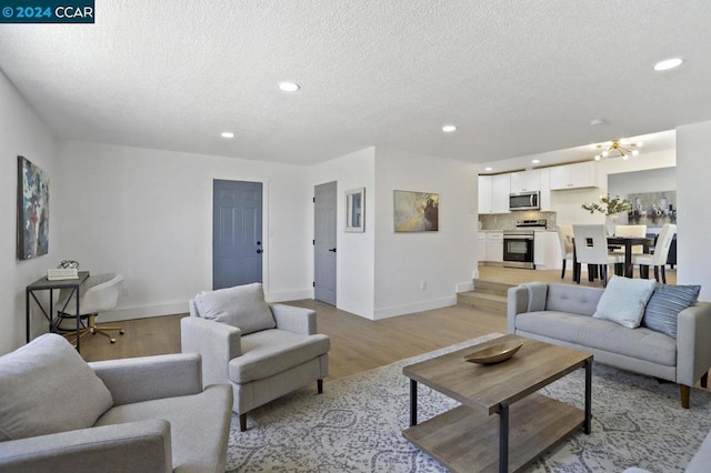 living room featuring light wood-type flooring, a textured ceiling, and an inviting chandelier