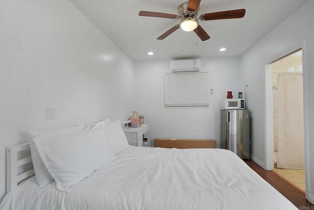 bedroom with ensuite bathroom, stainless steel refrigerator, an AC wall unit, ceiling fan, and wood-type flooring