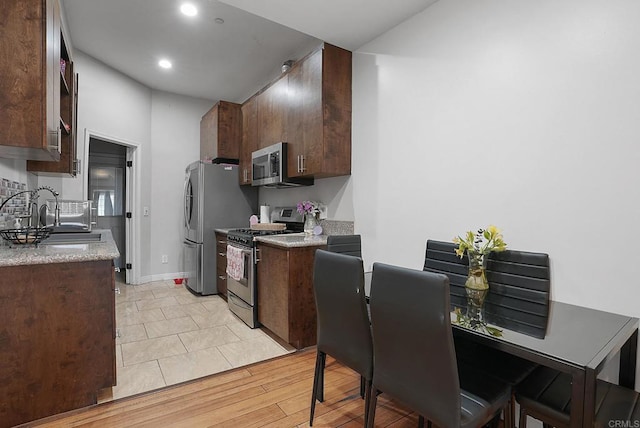 kitchen featuring stainless steel appliances, dark brown cabinetry, sink, and light wood-type flooring