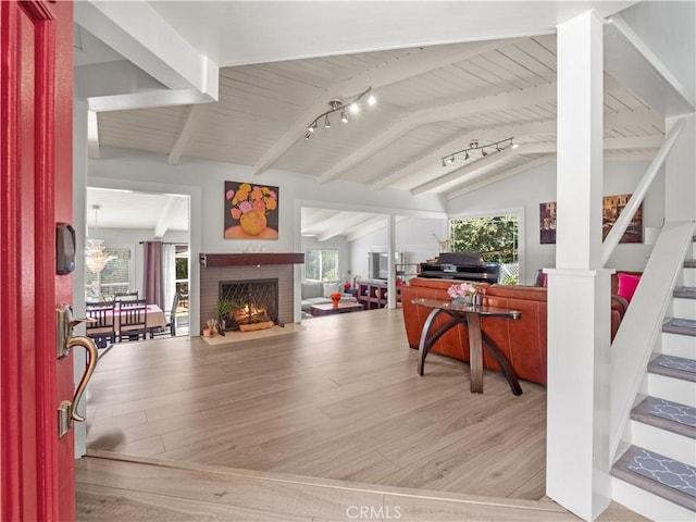 home office featuring lofted ceiling with beams, rail lighting, a brick fireplace, and light wood-type flooring