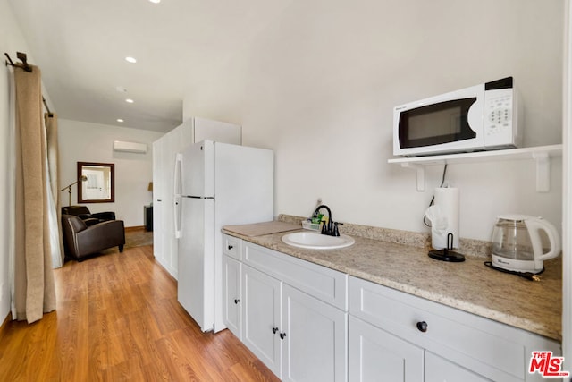 kitchen featuring a wall mounted AC, light hardwood / wood-style flooring, sink, white cabinetry, and white appliances