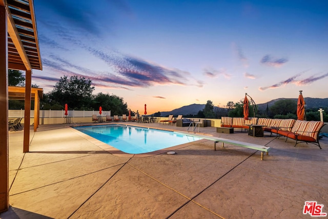 pool at dusk featuring a diving board, a patio area, and a mountain view