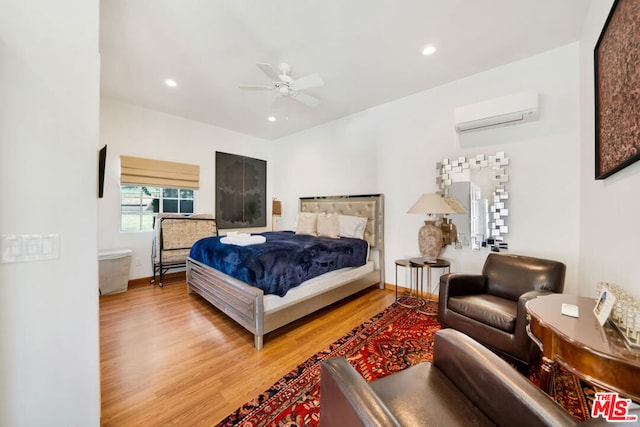 bedroom with ceiling fan, an AC wall unit, and light wood-type flooring