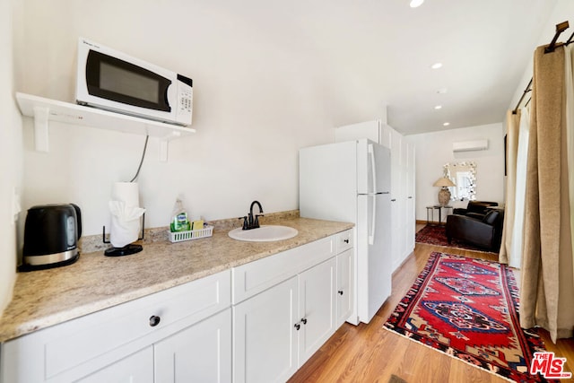 kitchen featuring a wall unit AC, sink, light wood-type flooring, white cabinetry, and white appliances