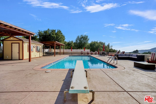 view of swimming pool featuring a shed, a diving board, an outdoor hangout area, a patio area, and a mountain view