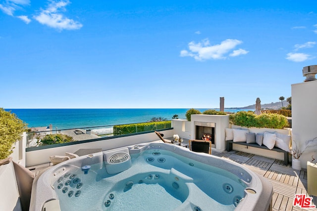 view of pool with a beach view, a water view, a hot tub, and an outdoor fireplace