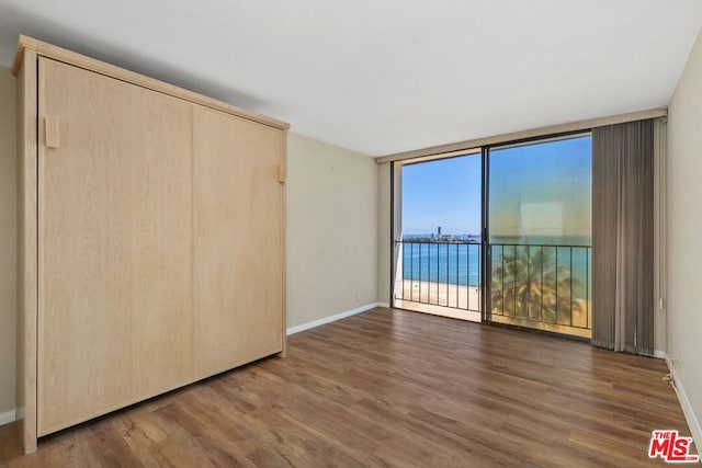 unfurnished bedroom with floor to ceiling windows, dark wood-type flooring, and a water view