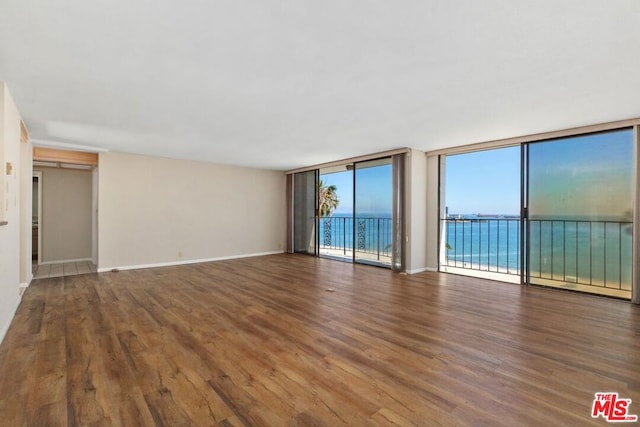 unfurnished room featuring dark wood-type flooring, a water view, and a wall of windows