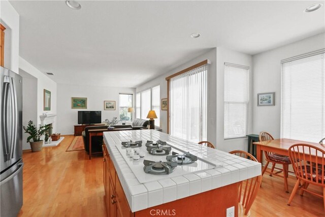 kitchen with open floor plan, a center island, freestanding refrigerator, tile countertops, and light wood-style floors