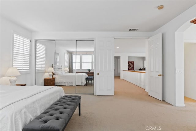 bedroom with visible vents, light carpet, arched walkways, and a closet