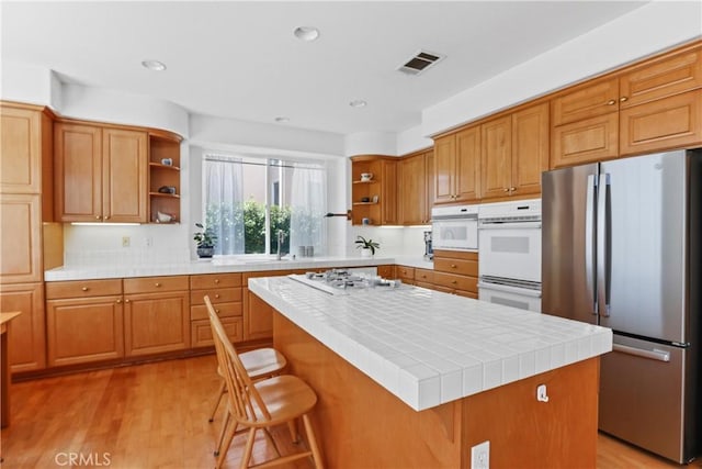 kitchen with light wood finished floors, visible vents, a kitchen island, white appliances, and open shelves