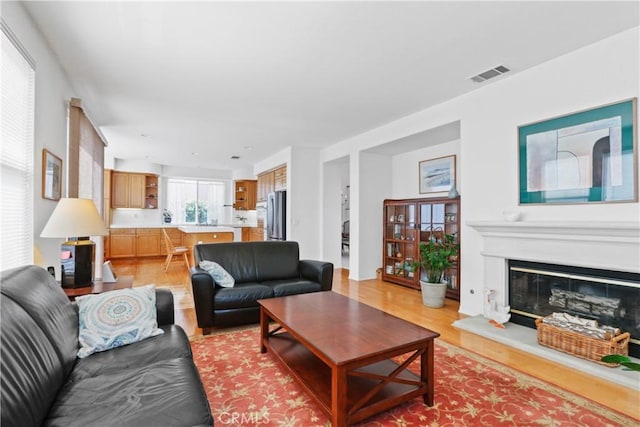 living area with a glass covered fireplace, light wood-style flooring, and visible vents