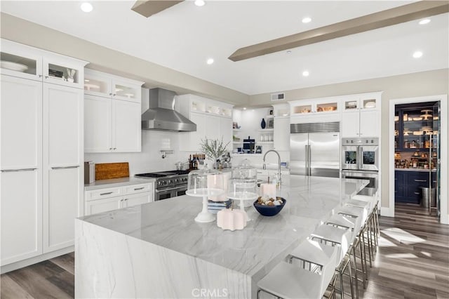 kitchen featuring visible vents, premium appliances, recessed lighting, wall chimney range hood, and a large island with sink