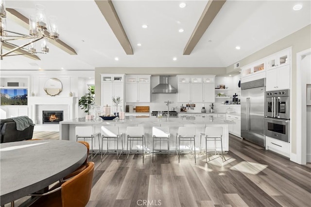 kitchen featuring wall chimney range hood, a breakfast bar area, a large island, stainless steel appliances, and open shelves