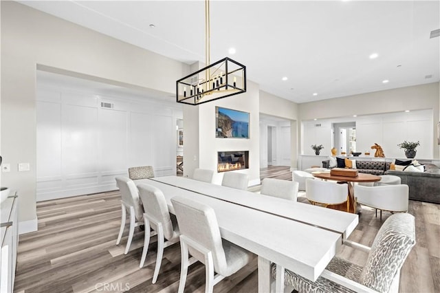 dining room featuring visible vents, recessed lighting, light wood-style floors, a glass covered fireplace, and a decorative wall