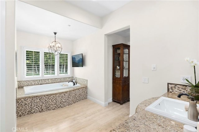 bathroom featuring baseboards, wood finished floors, a bath, a notable chandelier, and a sink