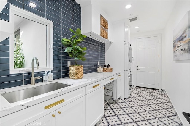 kitchen featuring white cabinets, light floors, stacked washer and clothes dryer, and a sink