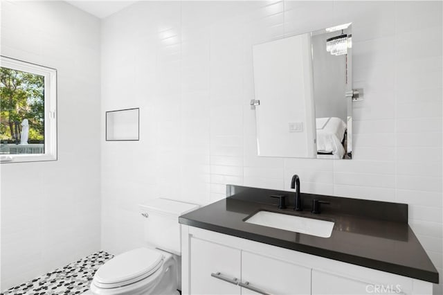 bathroom featuring toilet, vanity, a tile shower, decorative backsplash, and tile walls